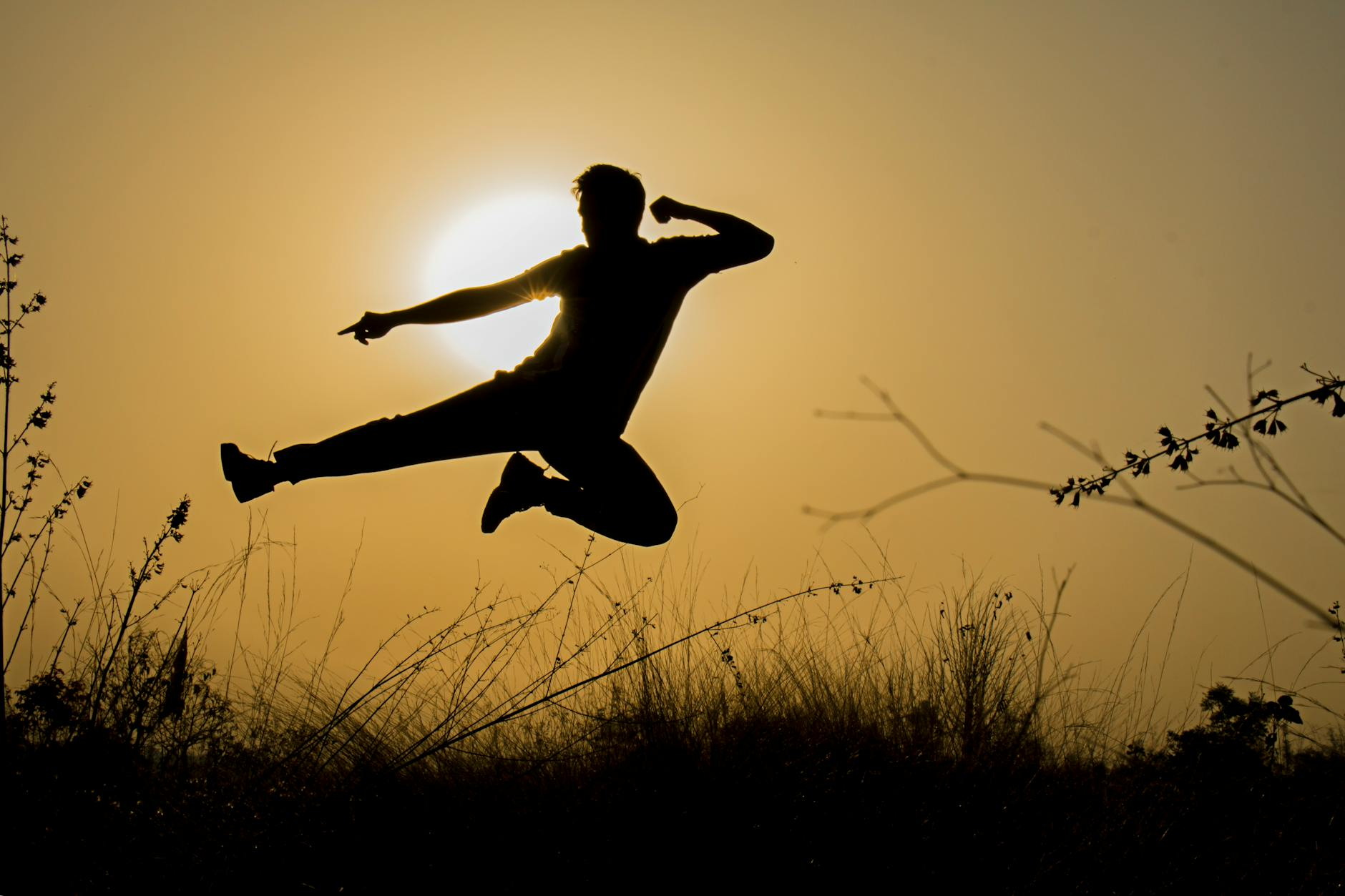 silhouette of man doing kick jump during sunset